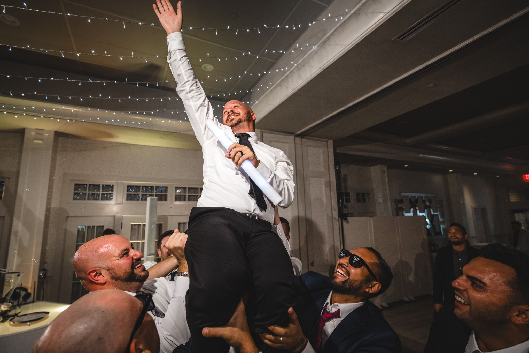 Party guests wave illuminated light sabers during an energetic wedding reception dance celebration.