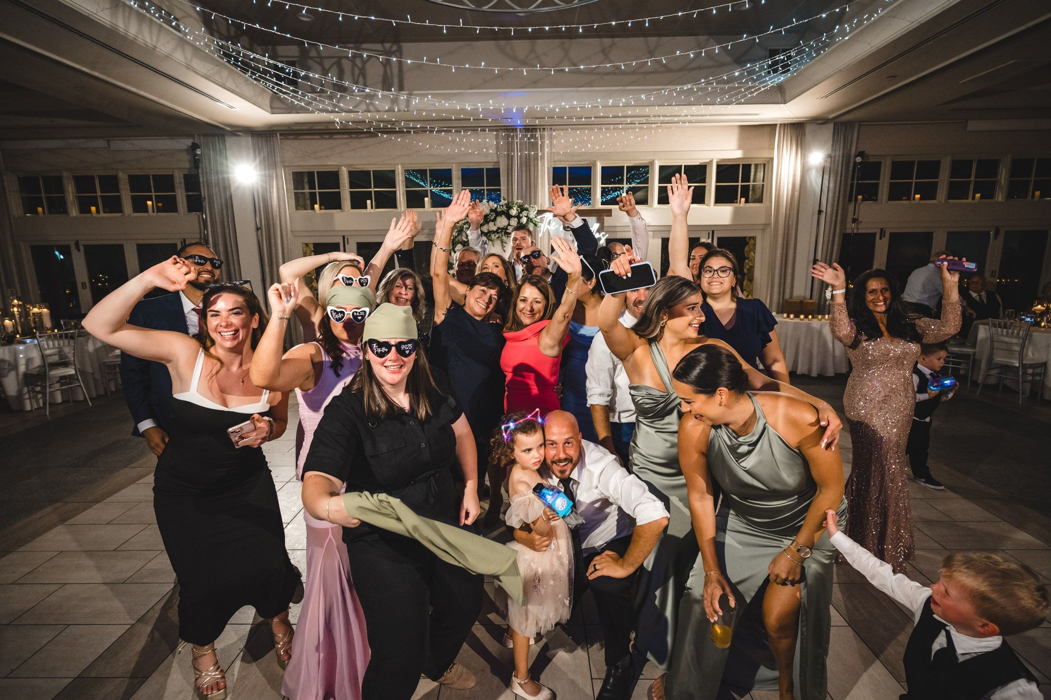 Wedding guests dancing and celebrating on a dance floor under twinkling lights.