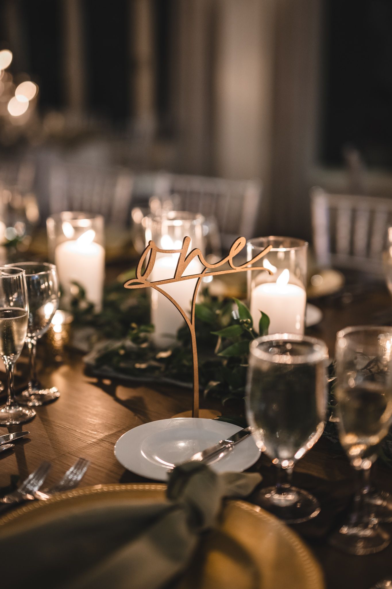 Romantic table setting with gold table number, candles, greenery and crystal glassware.