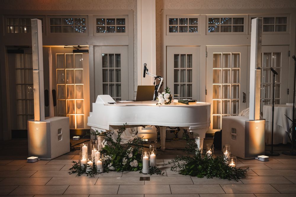 White grand piano decorated with candles and greenery for an elegant wedding ceremony setup.