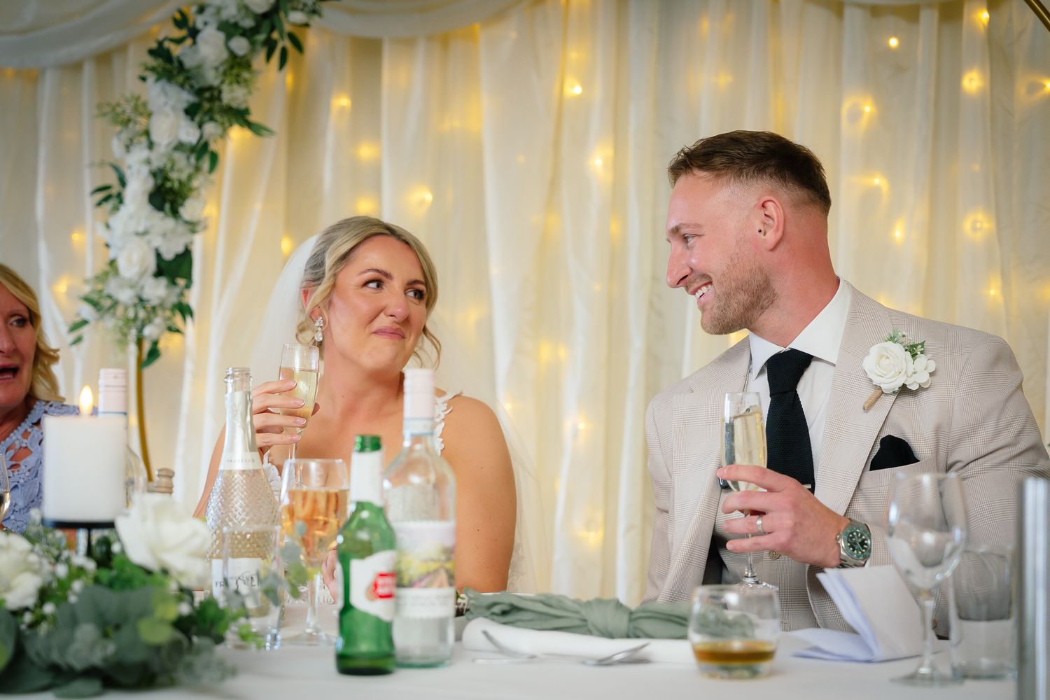 Wedding guests enjoy conversation and drinks at an elegant reception with soft lighting and floral decorations.