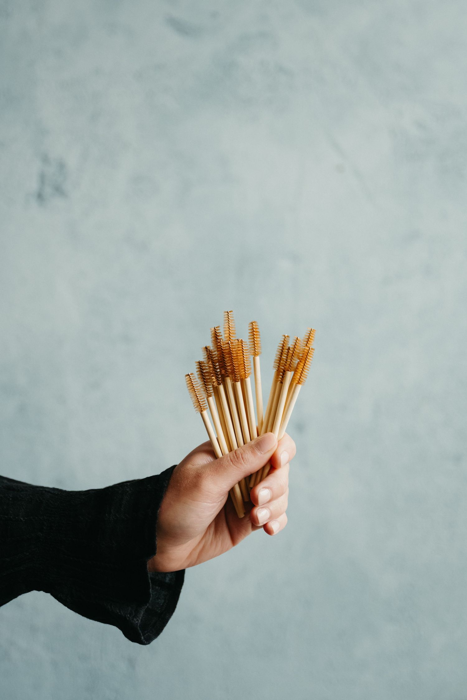 Hand holding a bundle of wooden chopsticks against a gray background in a sequence of progressively smaller amounts.