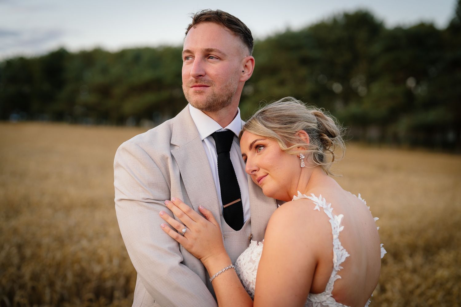 Romantic wedding couple embraces in golden wheat field at sunset.