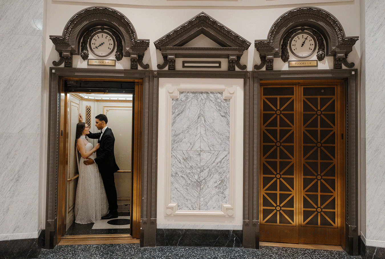 A romantic couple embraces in an elegant marble hallway with ornate wooden doors and decorative wall panels.