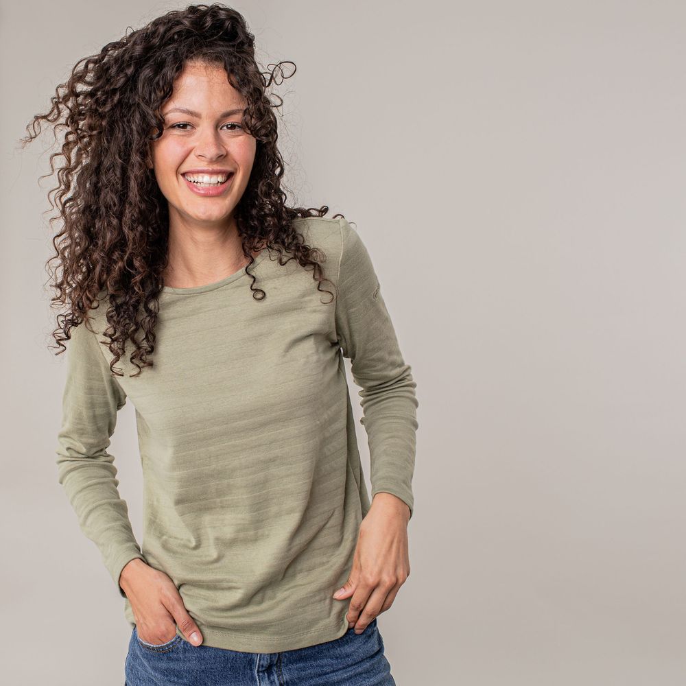 Person with curly dark hair wearing a sage green sweater and blue jeans poses in multiple casual stances.