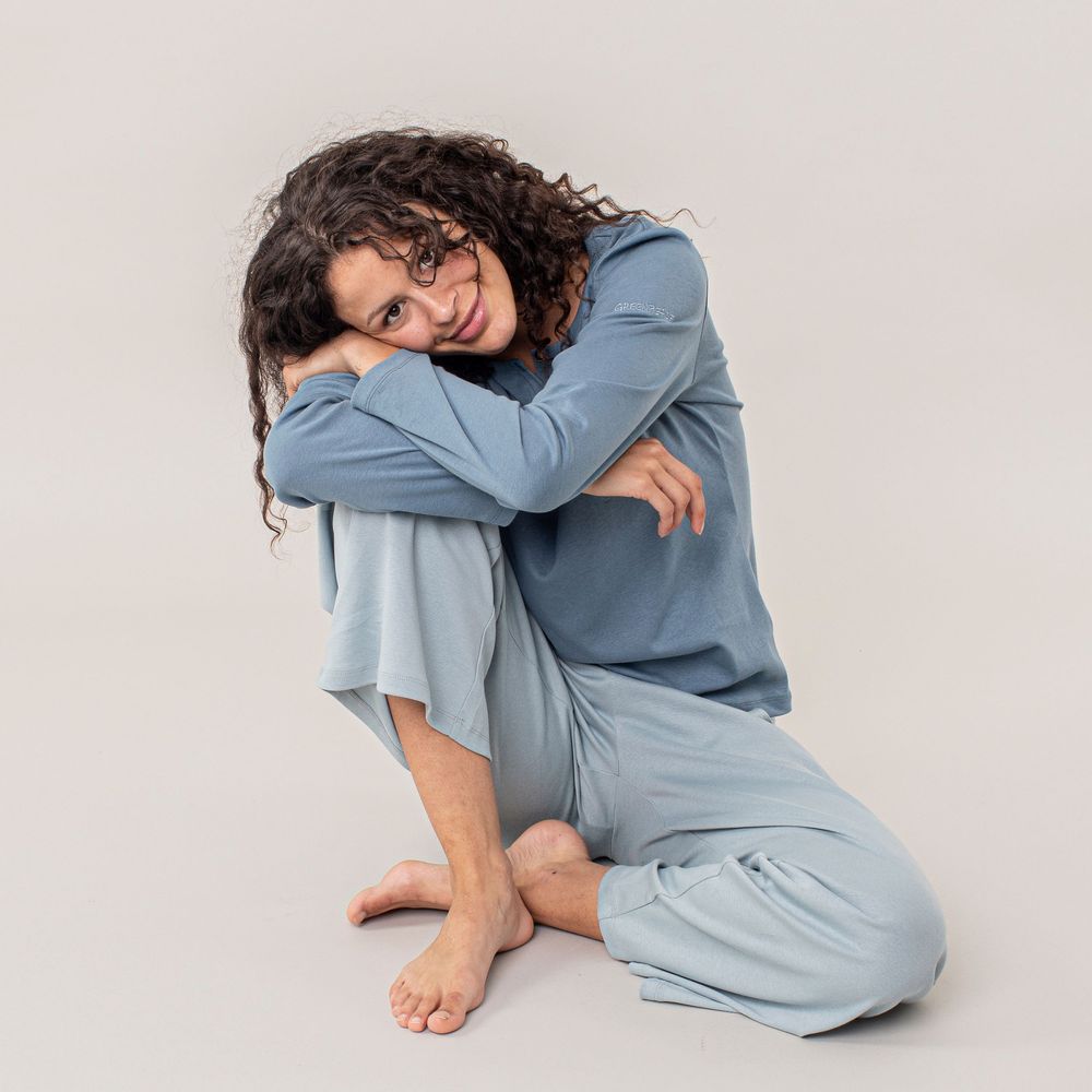 Person in light blue loungewear lies curled up on white background in artistic poses showing comfort and relaxation.