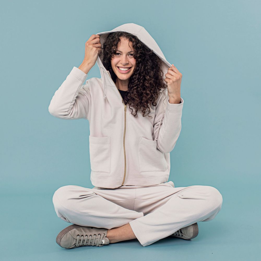 Person in cozy white loungewear sits and poses playfully against light blue background in photo series.