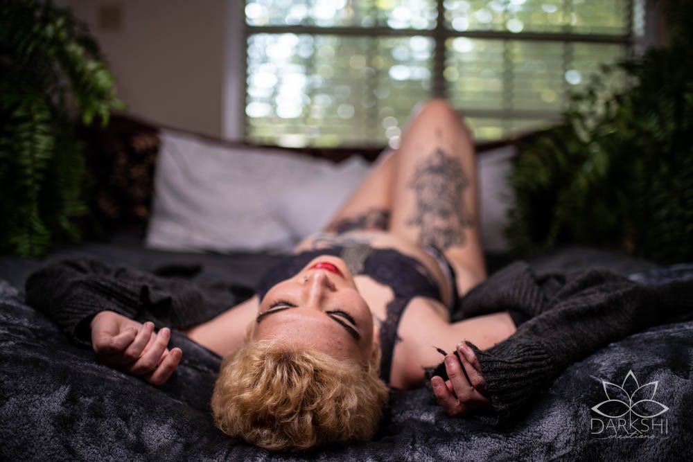 Person lying on dark fabric with soft window light creating atmospheric mood.