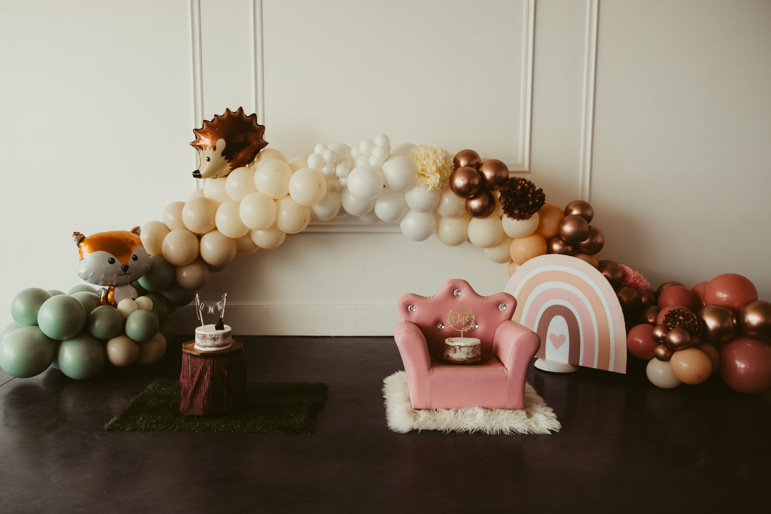Festive first birthday cake smash setup with woodland animal balloons and pink throne chair.