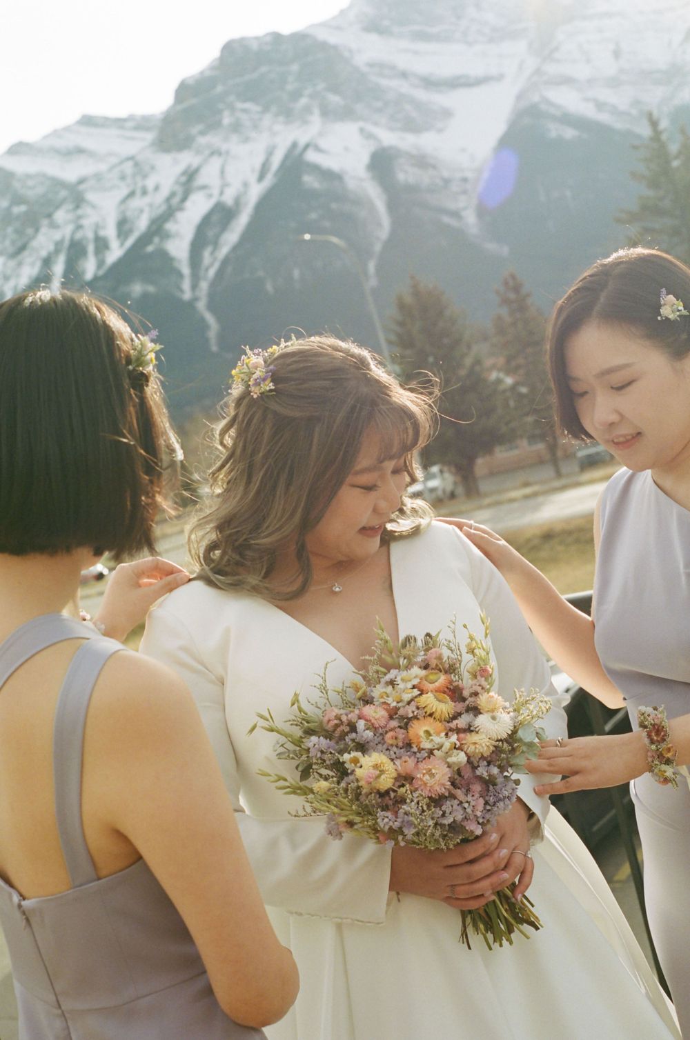 A wedding party stands against a stunning mountain backdrop in the Canadian Rockies holding delicate floral bouquets.