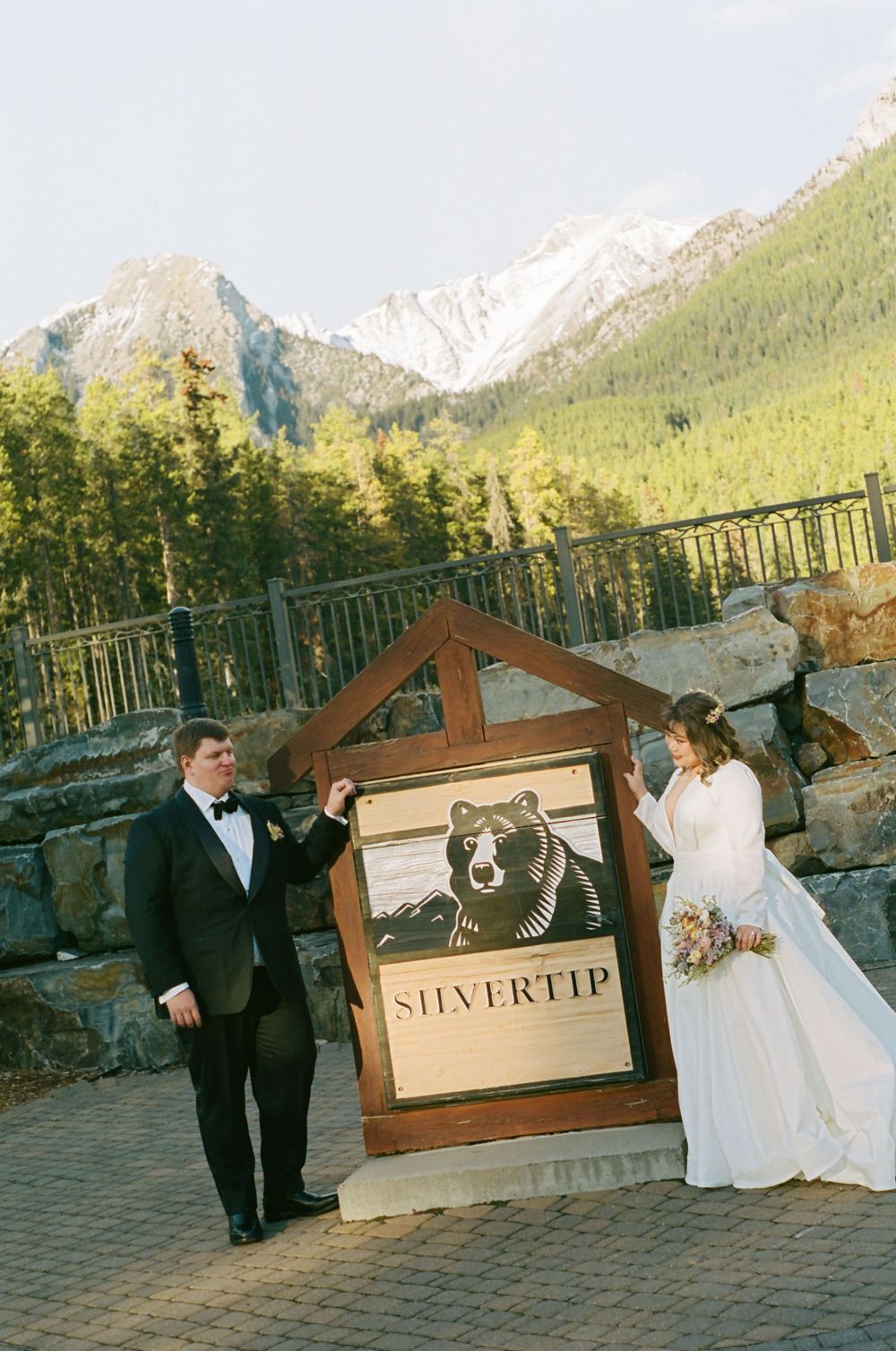 Newlyweds pose near a Silvertip resort sign with majestic mountains in the background.