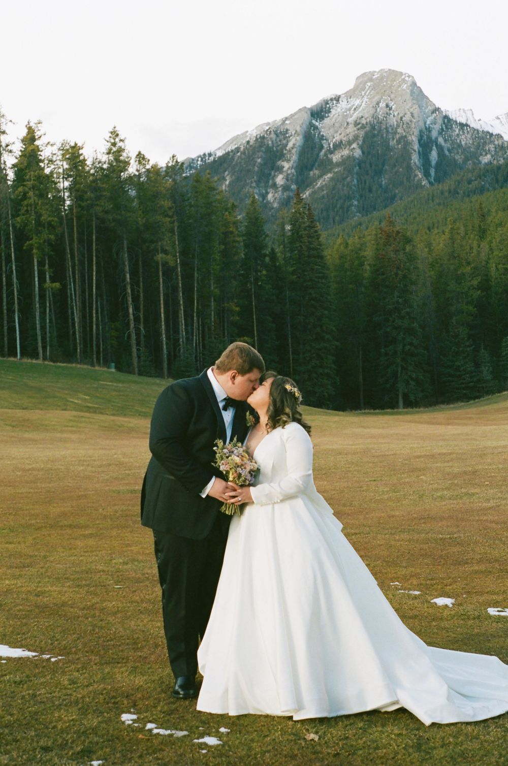 Wedding couple sharing a romantic moment in front of a mountain landscape with evergreen trees.