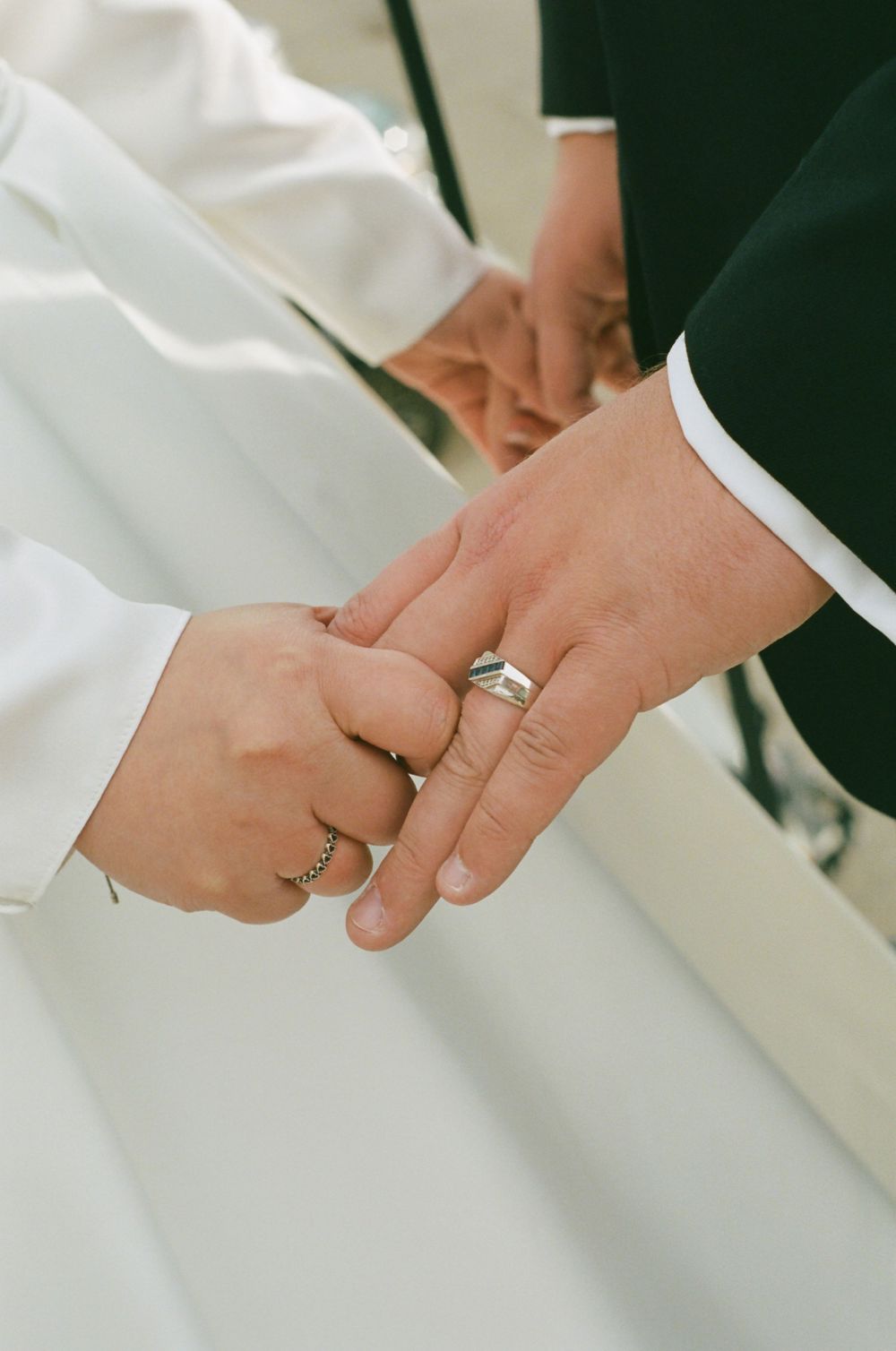 Close-up shot of hands with wedding rings against white and dark fabric backgrounds.