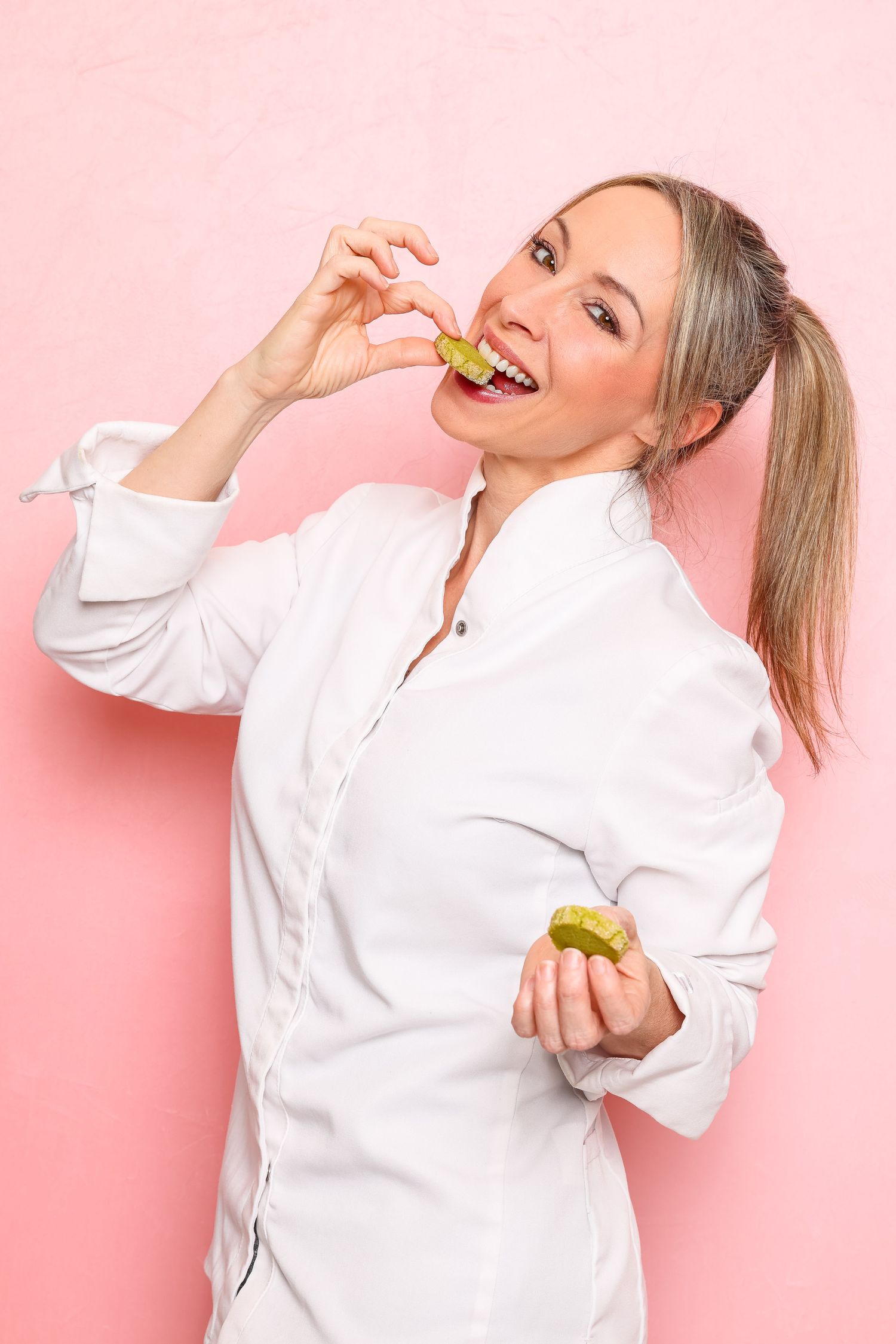 Professional chef in white uniform holds a fresh strawberry cheesecake against pink background.