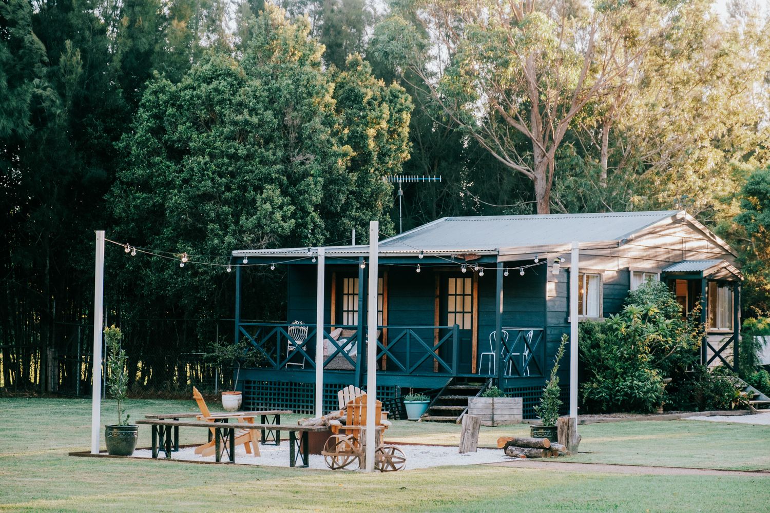 Panoramic view of a rustic campground with covered picnic areas and wooden structures nestled among tall trees.