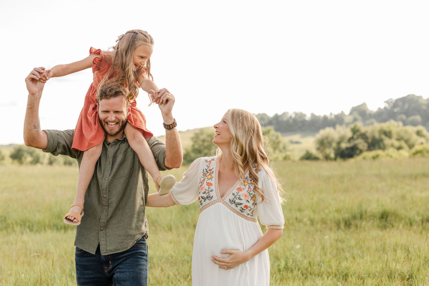 Happy family with pregnant mother, father, and daughter in sunny green field.