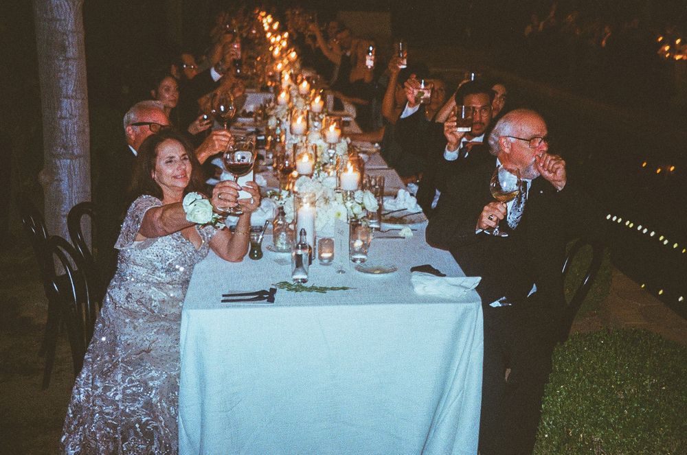 Wedding reception guests enjoying dinner at elegantly decorated outdoor tables with glowing lights in the evening.