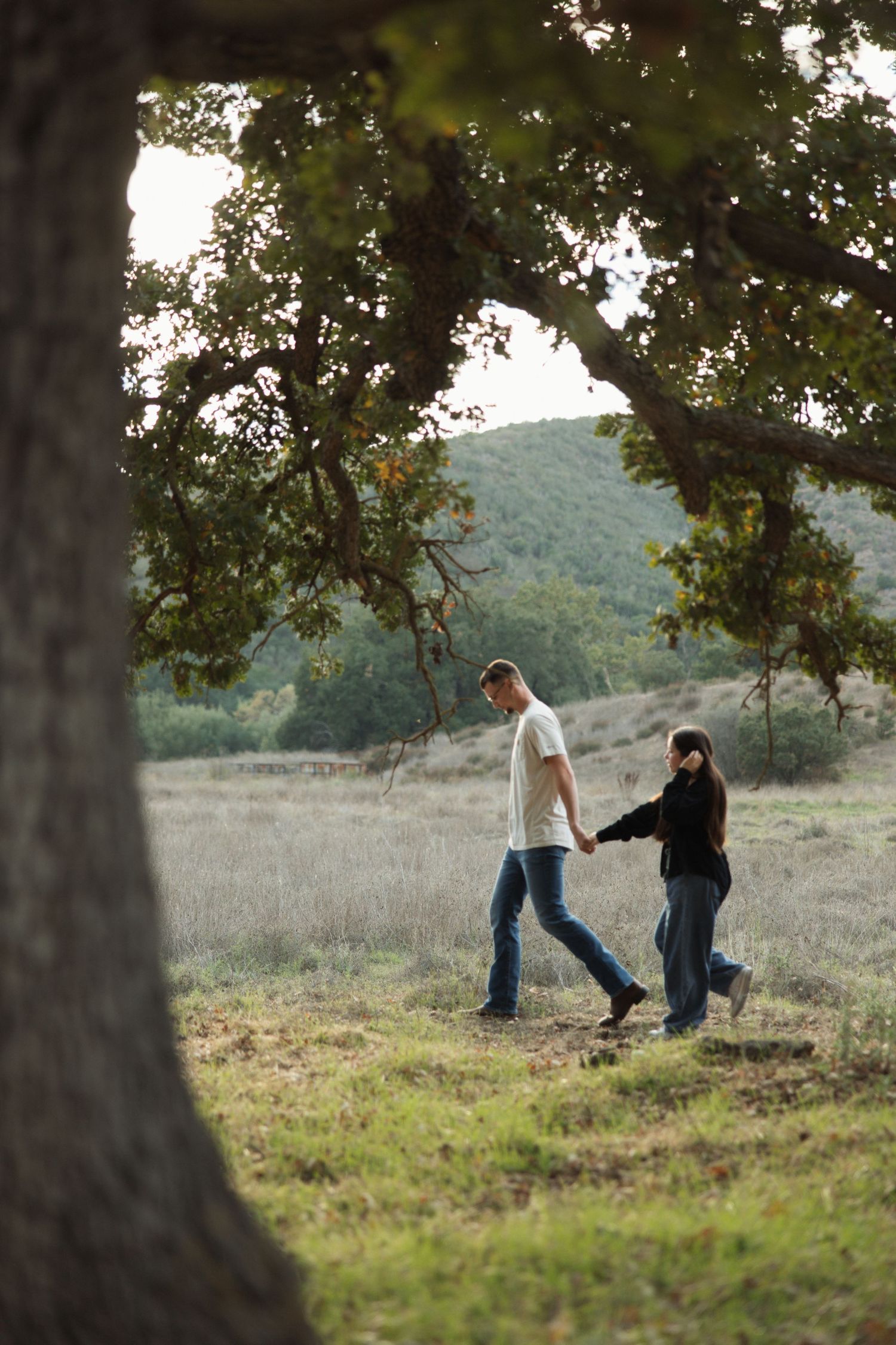 Engagement session in Agoura Hills with a couple walking around an oak tree at sunset