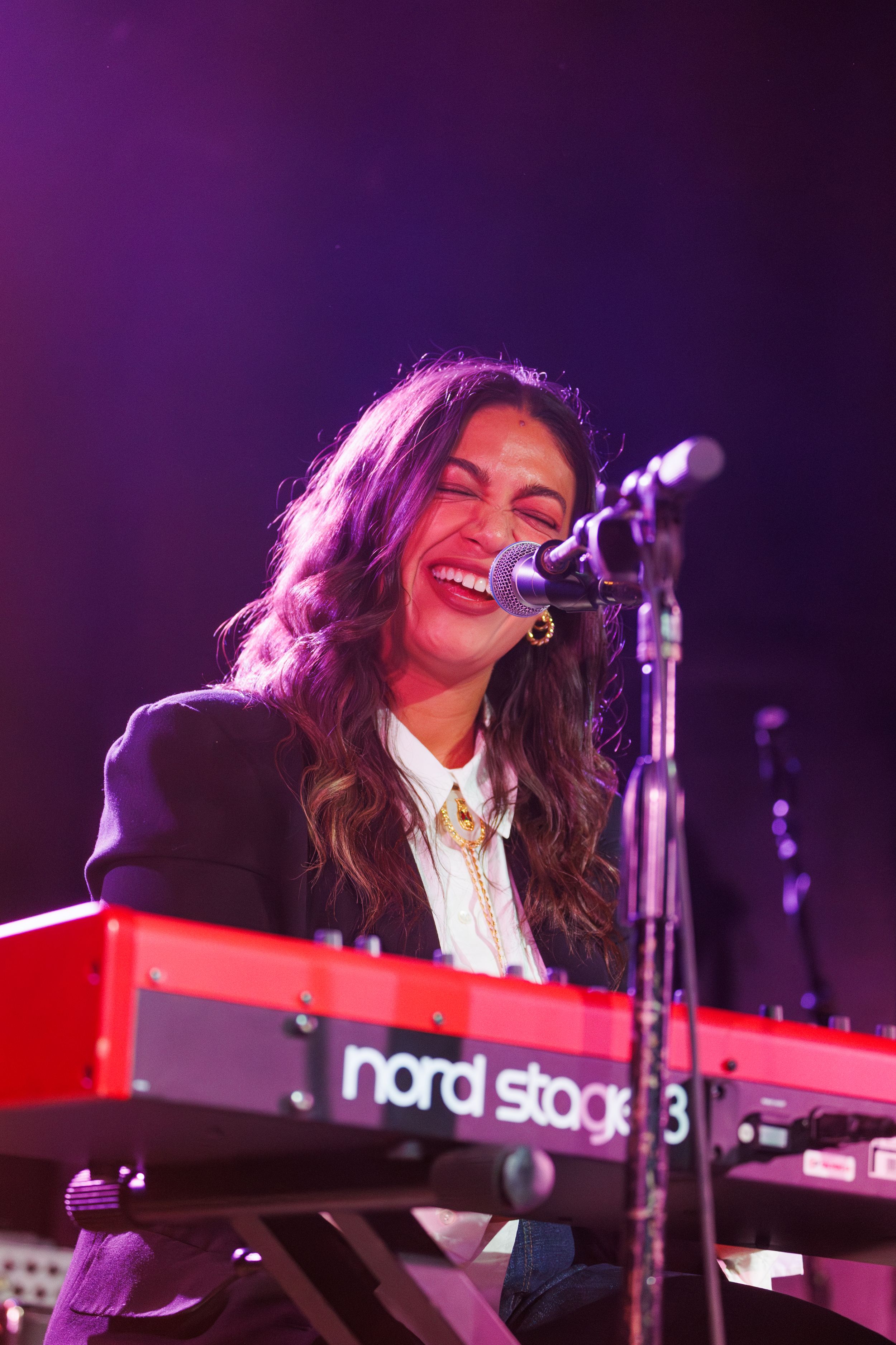 Musician performs on stage at a Nord Stage 3 keyboard under purple lighting during a concert performance.
