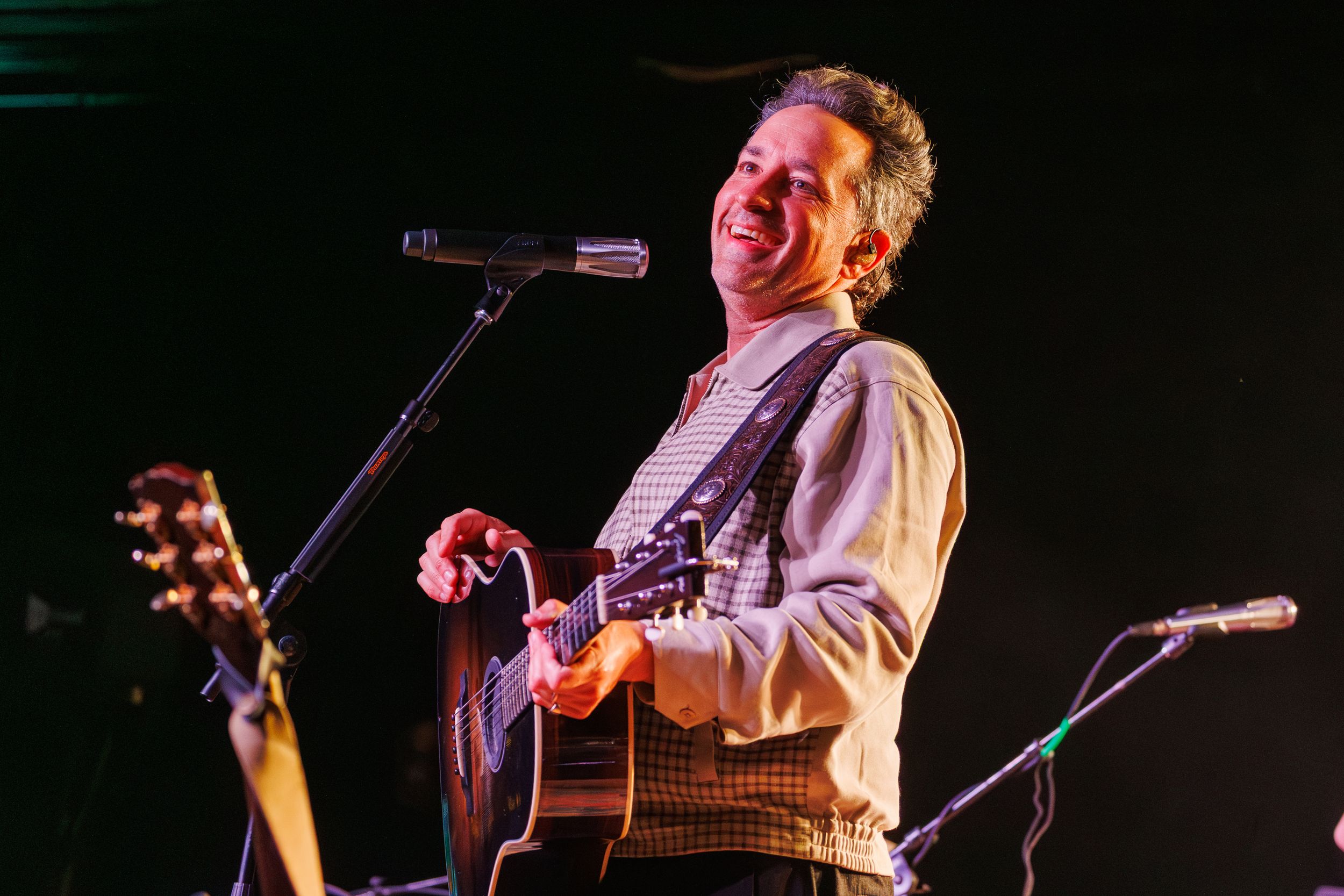 A performer sings and plays acoustic guitar on stage under dramatic lighting during a concert performance.