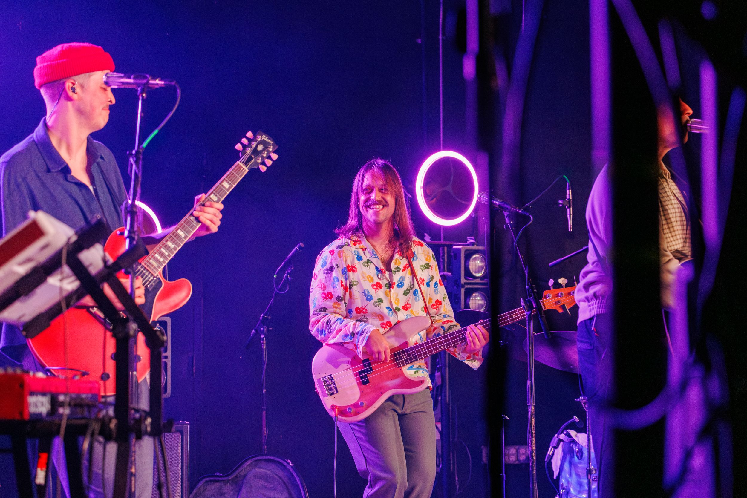 Musicians perform on stage with purple and blue lighting effects during a live concert performance.