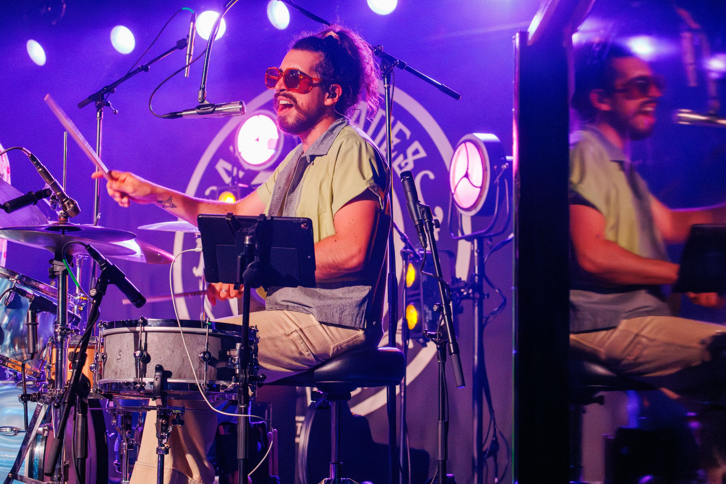 Musicians perform on stage with purple and blue lighting creating an energetic concert atmosphere.