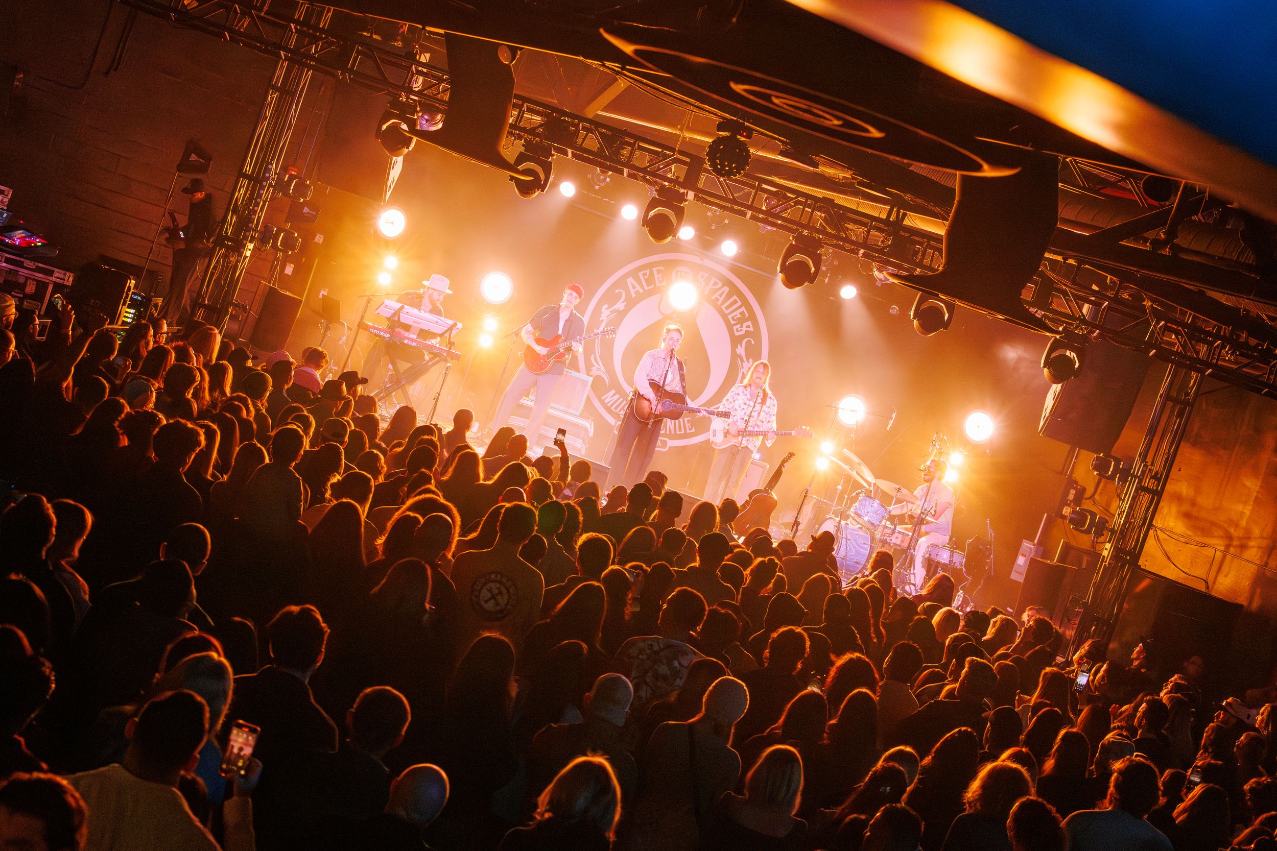 Silhouetted crowd watching a concert with warm orange stage lighting creating an atmospheric ambiance.