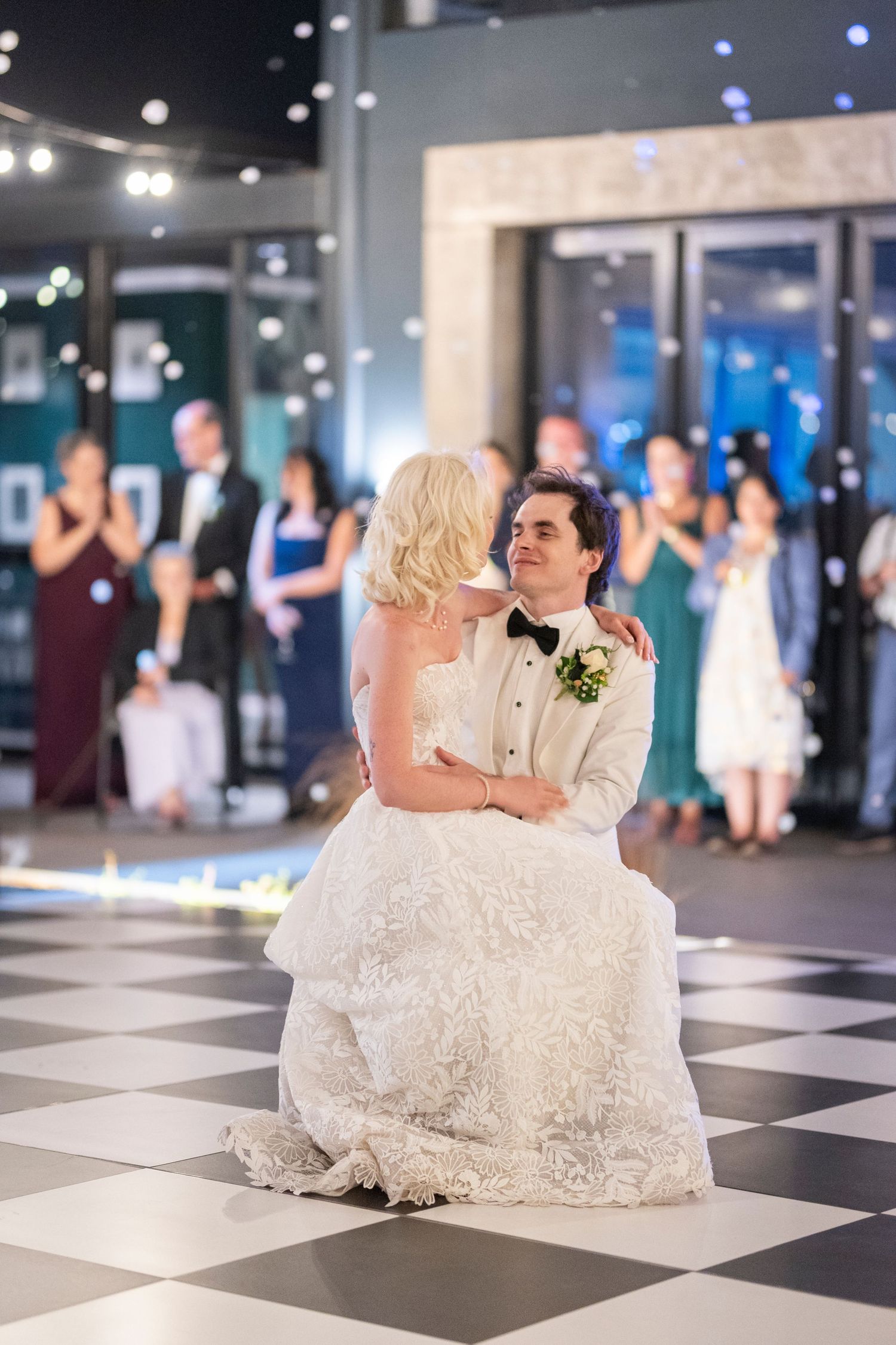 A couple shares their first dance on a black and white checkered dance floor at an elegant wedding reception.