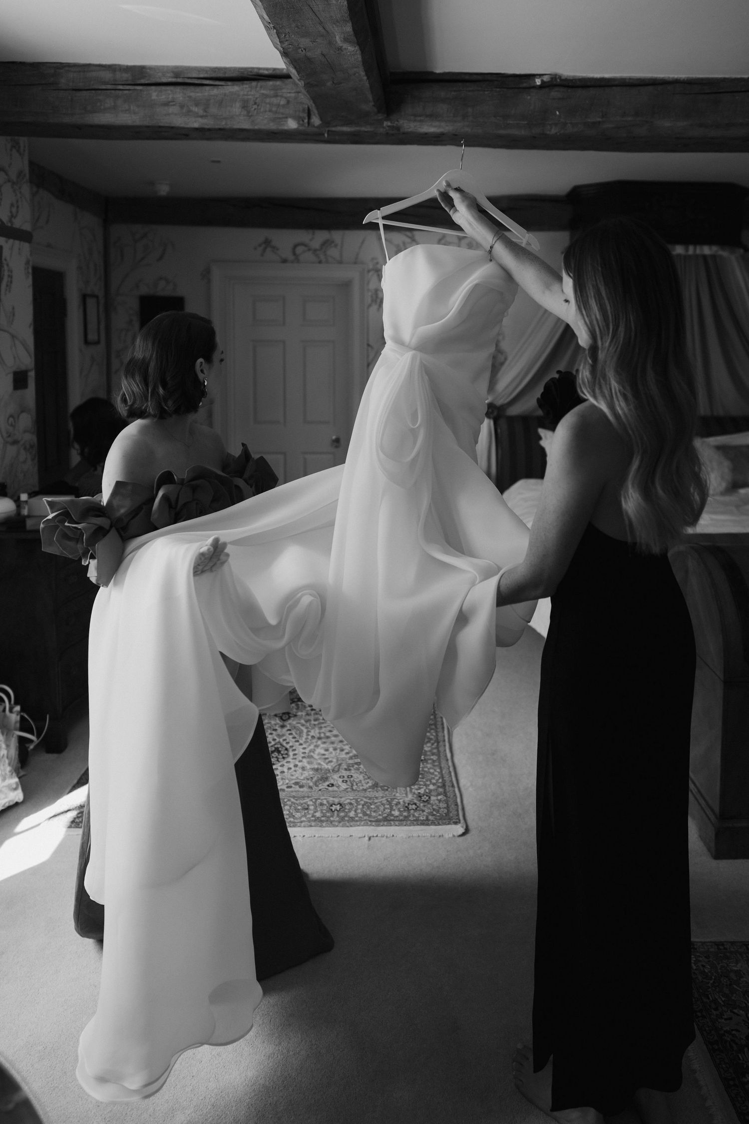 sister and friend lifting wedding dress off hanger before bride gets dressed at dewsall court in herefordshire
