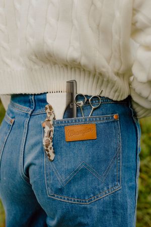 Close-up of Wrangler jeans back pocket with scissors, comb, and hair clip tucked inside.