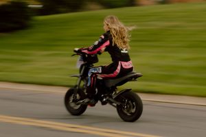 Blonde woman riding black and pink motorcycle on road with motion blur background.
