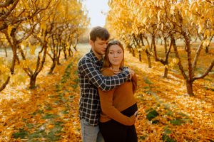 Couple embracing in golden autumn orchard with yellow fallen leaves on ground.