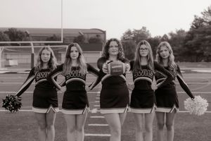 Five high school cheerleaders in black uniforms posing on football field in black and white photo.