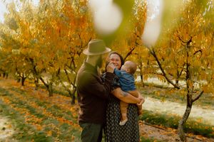Family portrait with couple holding baby among golden autumn trees.