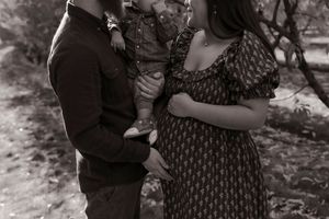 Black and white photo of a couple with toddler and pregnant belly on a garden path.