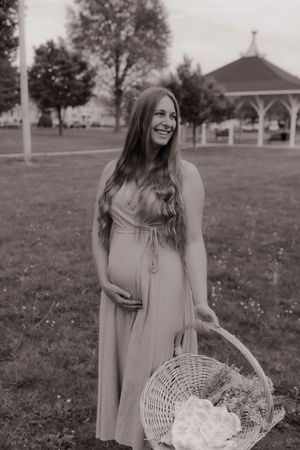 Black and white portrait of smiling pregnant woman holding flower basket in park.