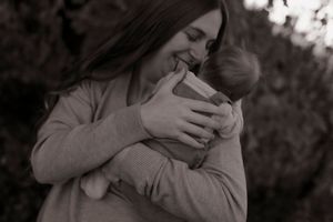 Black and white portrait of a smiling mother tenderly cradling her newborn baby outdoors.
