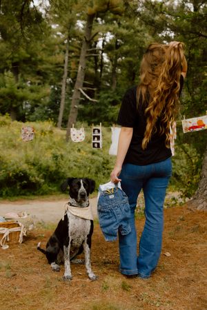 Woman holding tiny jeans beside a black and white dog outdoors with ultrasound photos hanging on a line.