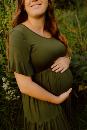 Pregnant woman in olive green dress cradling baby bump in garden setting.
