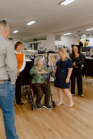 Group of people gathered around elderly woman in wheelchair inside retail store.