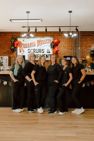 Six women in black scrubs posing together at Redding Medical Scrubs and Equipment store.