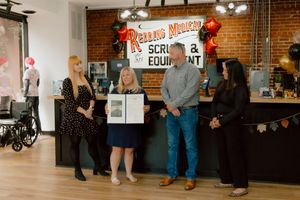 Four people stand indoors at Reading Medical Scrubs and Equipment store during an award presentation ceremony.