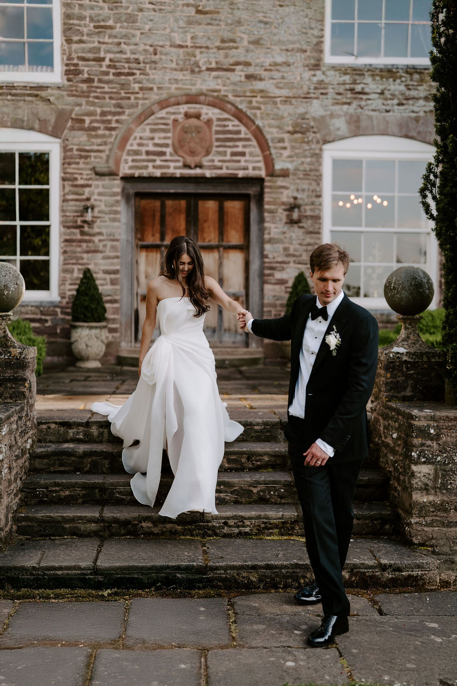 groom holding brides hand, leading bride down the stairs outside dewsall court in herefordshire