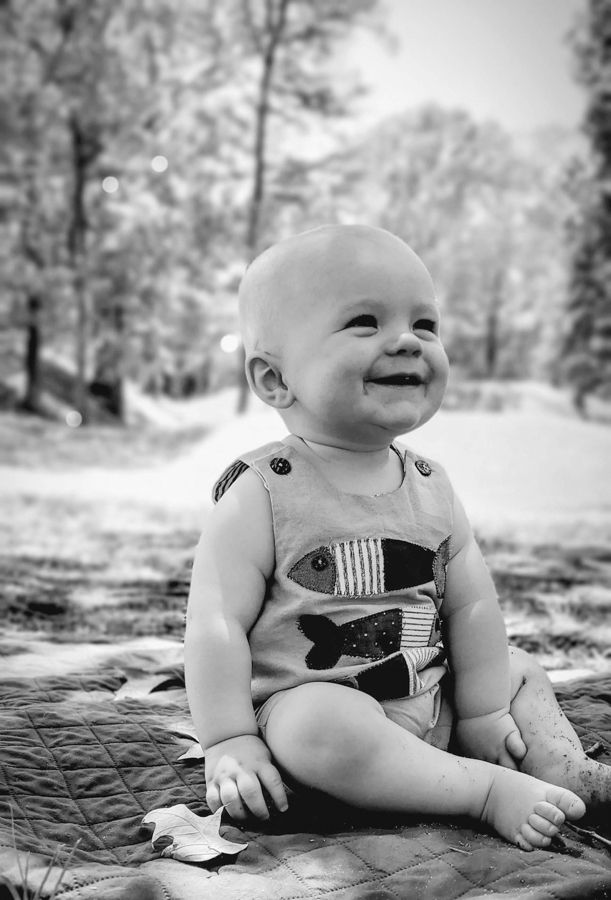 baby boy in an open grassy area smilingt wearing a fishy short coverall