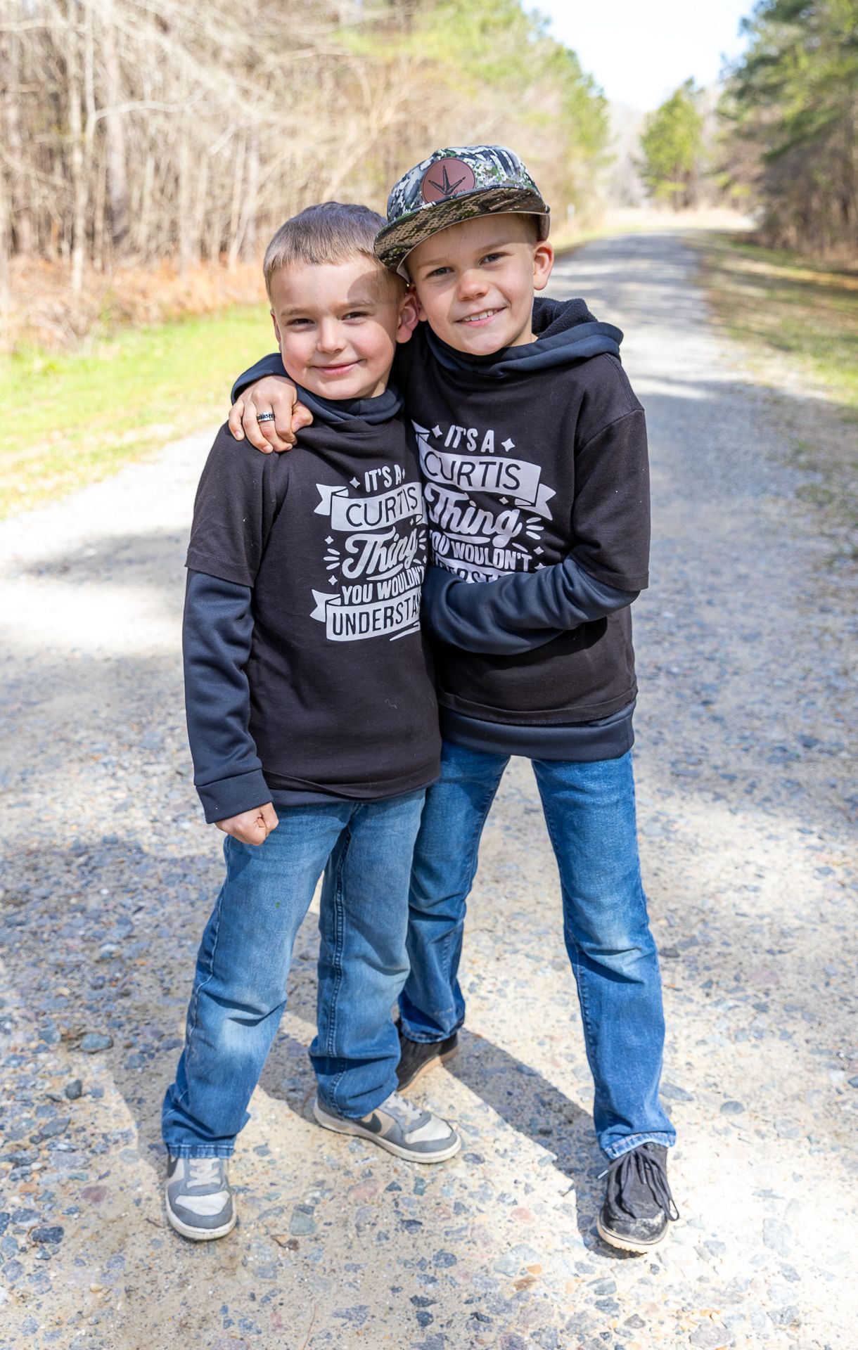 Two brothers in matching Curtis hoodies hugging on a gravel road.