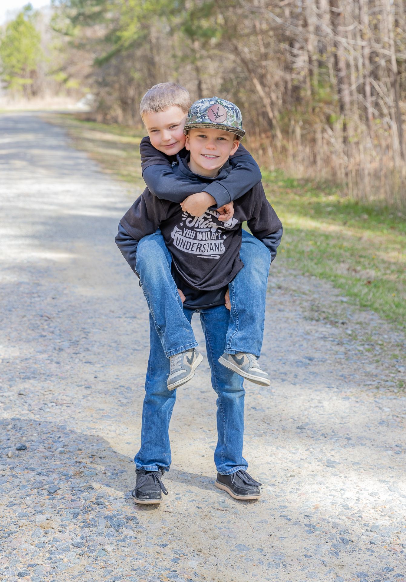 Older boy giving younger brother a piggyback ride on a dirt path.