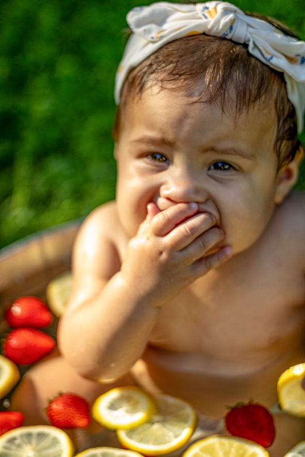 milestones session
baby girl eating a strawberry looking right at us
in a strawberry lemon bath in afternoon light