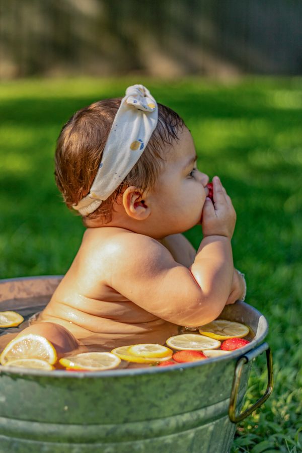 baby girl naked in a strawberry lemon tub with a lemon headband
baby rolls showing while she eats a strawberry in the afternoon sunlight