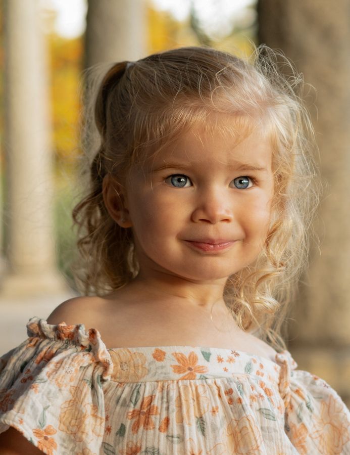 Portrait of curly blonde toddler girl with blue eyes in floral dress.