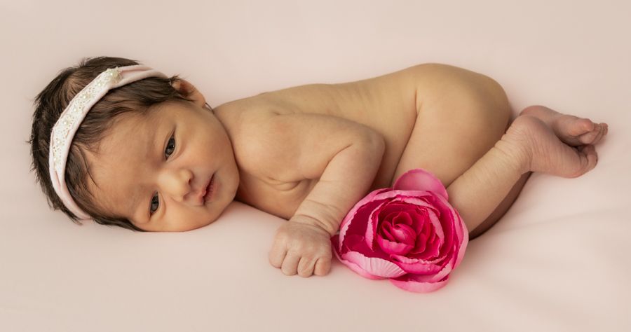 newborn baby girl curled up naked with a pink peony flower and a light pink head band